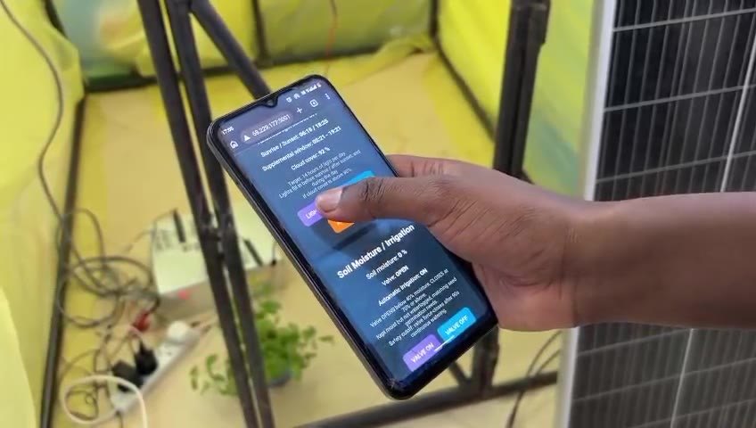 Phone running the Bonita dashboard beside the greenhouse and its solar panel